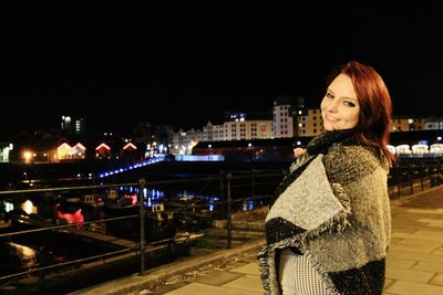 Side view portrait of smiling woman wrapped in blanket standing against sky at night