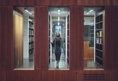 Portrait of young woman seen through window standing at library