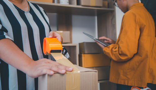 Midsection of woman packing box with girl working over digital tablet