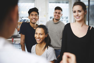 Happy multi-ethnic students looking at female teacher in chemistry laboratory