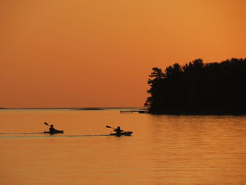 Silhouette people in boat on sea against orange sky during sunset