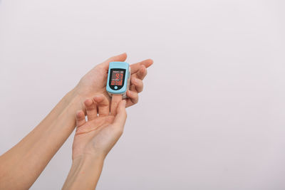 Cropped hands of woman holding remote control against white background