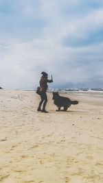 Man with dog standing on beach against sky