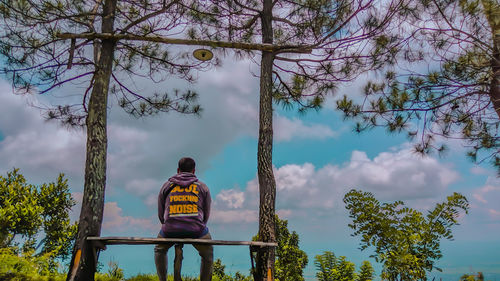 Rear view of man standing by trees against sky