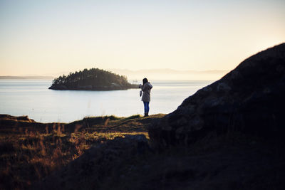 Man standing on rock by sea against sky during sunset