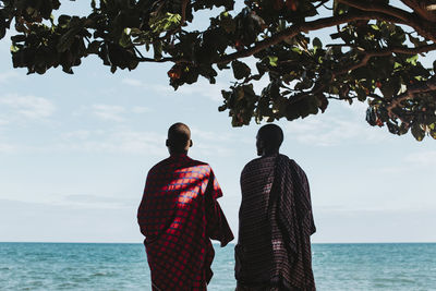 Two masai men in traditional clothes standing under big mkungu tree