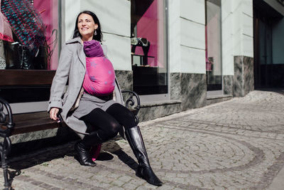 Full length of woman carrying son in scarf on bench