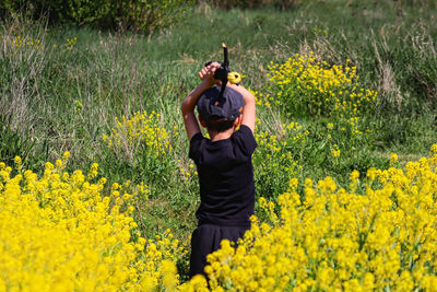 Rear view of woman standing amidst yellow flowering plants on field