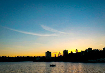 Silhouette buildings by river against sky during sunset