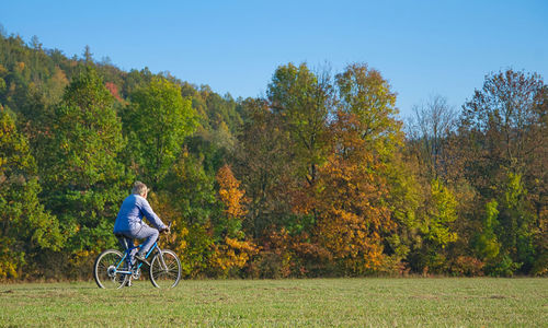 Side view of senior man riding bicycle on land by trees