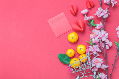 High angle view of fruits in shopping cart by flowers over pink background