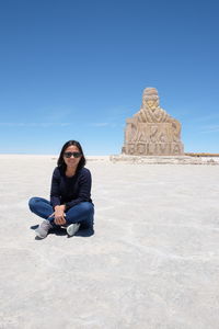 Young woman sitting on land against clear blue sky