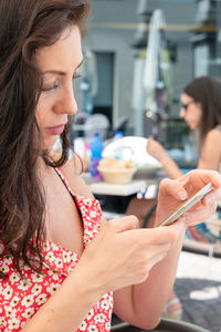 Mid adult woman using smart phone while sitting at sidewalk cafe