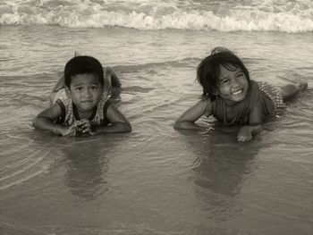 Portrait of cheerful siblings lying on sea shore at beach