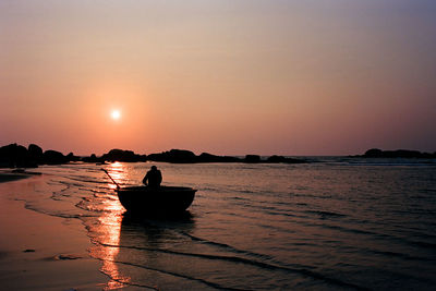 Silhouette man sitting on boat in sea against sky during sunset