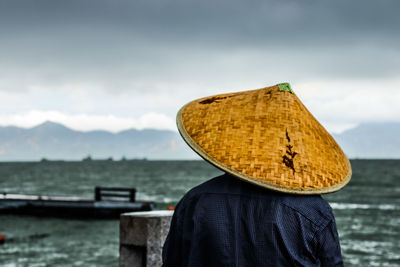 Rear view of men wearing asian style conical hat at beach against sky
