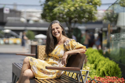 Happy mature woman sitting on bench during sunny day