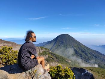 Side view of man sitting on rock against mountain