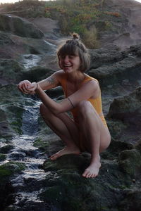 Portrait of young woman sitting on rock smiling nature