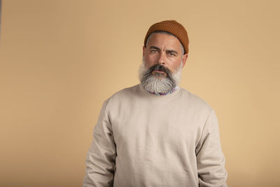 Portrait of a handsome bearded man looking seriously at the camera over beige background.