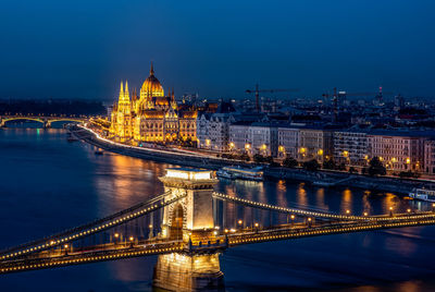 Illuminated bridge over river in city at night