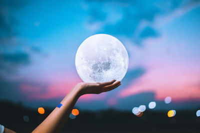 Close-up of hand holding lighting equipment against sky during sunset