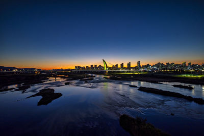 River by illuminated city against sky at sunset