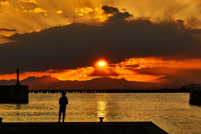 Silhouette man standing by sea against sky during sunset