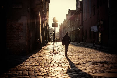 Rear view of man walking on street amidst buildings in city