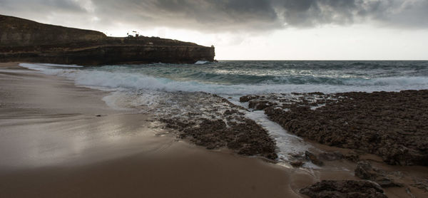 Scenic view of beach against cloudy sky