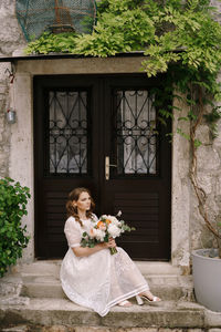 Bride holding bouquet sitting on steps by door