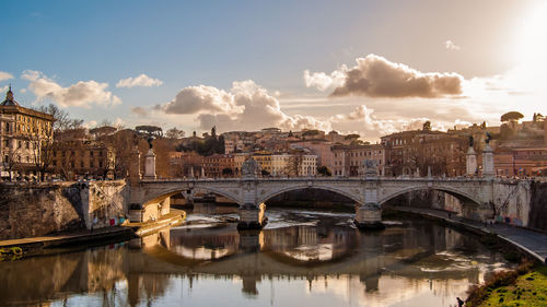 Arch bridge over river in city against sky