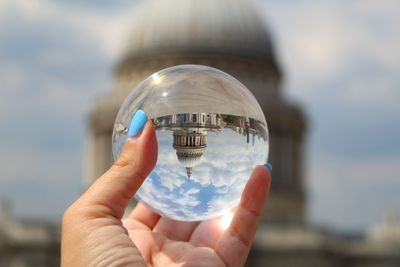 Cropped hand holding crystal ball against buildings