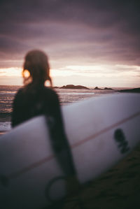 Woman standing by sea against sky during sunset