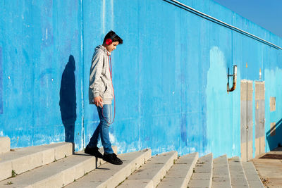Young teen listening music by headphones against blue wall