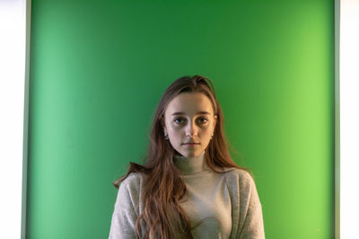 Portrait of young woman standing against green wall