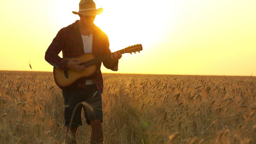 Man playing guitar on land against sky during sunset