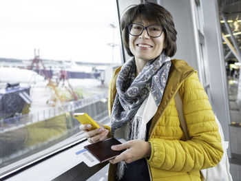 Smiling woman with passport and boarding pass is texting on her smartphone. 