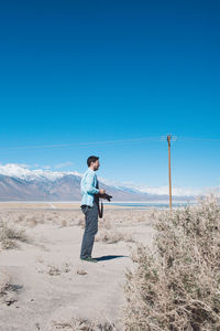 Full length of man photographing while standing in desert against clear blue sky