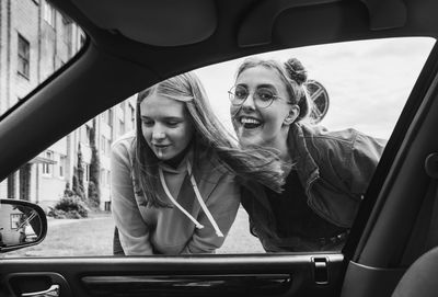 Portrait of 2 teenagers smiling against car window