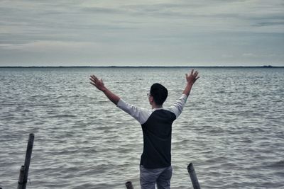 Rear view of man standing at sea shore against sky