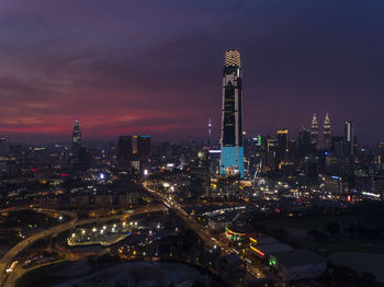 Illuminated modern buildings in city against sky at night