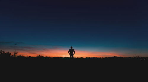 Silhouette man standing on field against sky during sunset