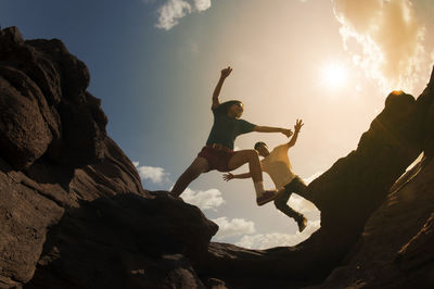 Low angle view of friends jumping over rock formations against sky