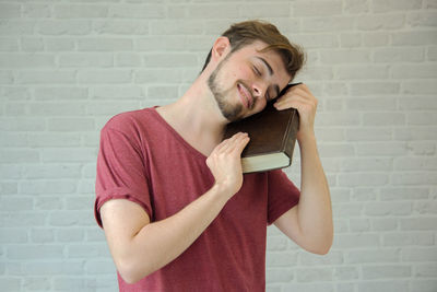 Smiling young man holding bible against wall