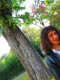 Portrait of young woman standing by tree trunk