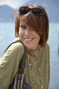 Close-up portrait of smiling young woman standing against lake