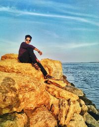 Man standing on rock by sea against sky