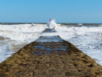 Waves splashing on pier against clear sky