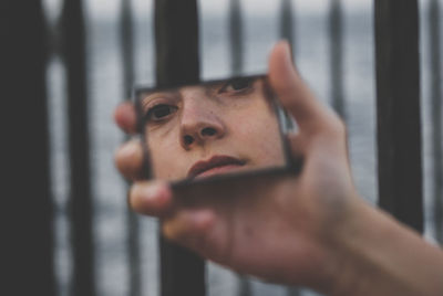 Close-up portrait of man holding cigarette against window